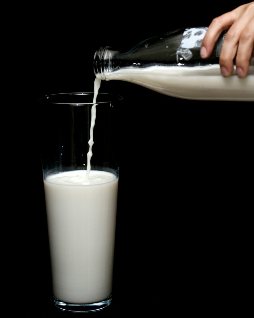 A hand pouring a glass of milk.